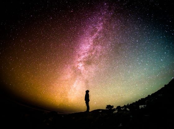 silhouette of person standing under colorful starry sky